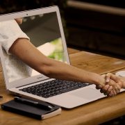 Person shaking hands with another person whose arm is reaching out from inside a computer screen